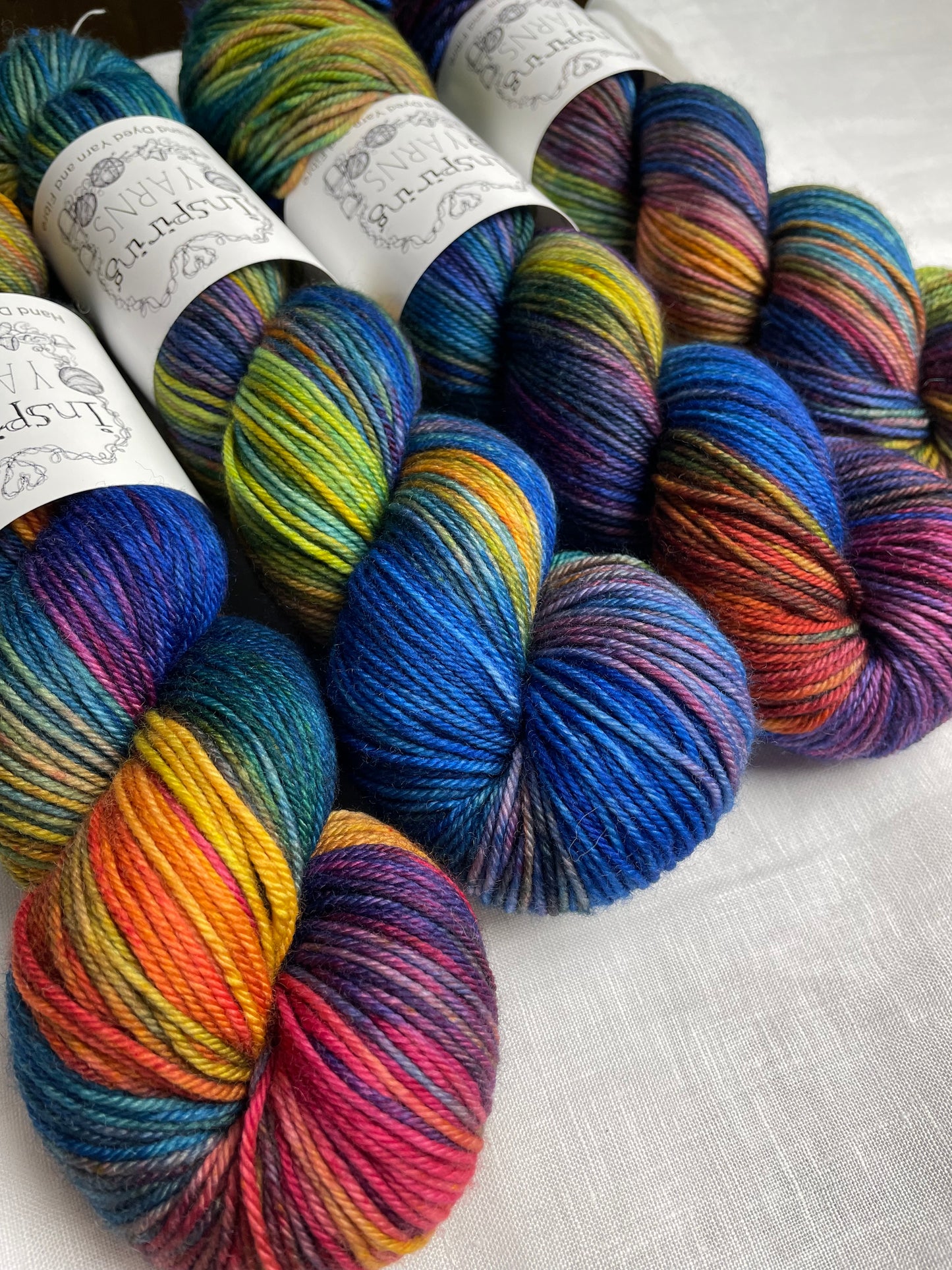 Four skeins of blue and multi coloured Merino Smooth DK yarn labelled Inspiring Yarns on a white linen background.
