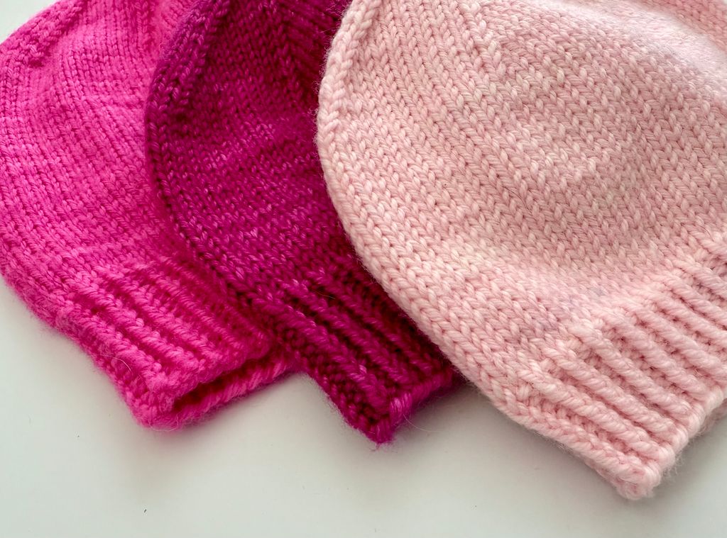 Two knitted hats, one pink and one magenta, on a light background.
