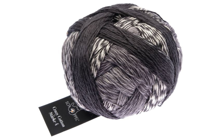 Image shows wound ball of Schoppel Crazy Cotton 4ply/sock. The colour is flight of the moon, with shades of black, grey and off-white.