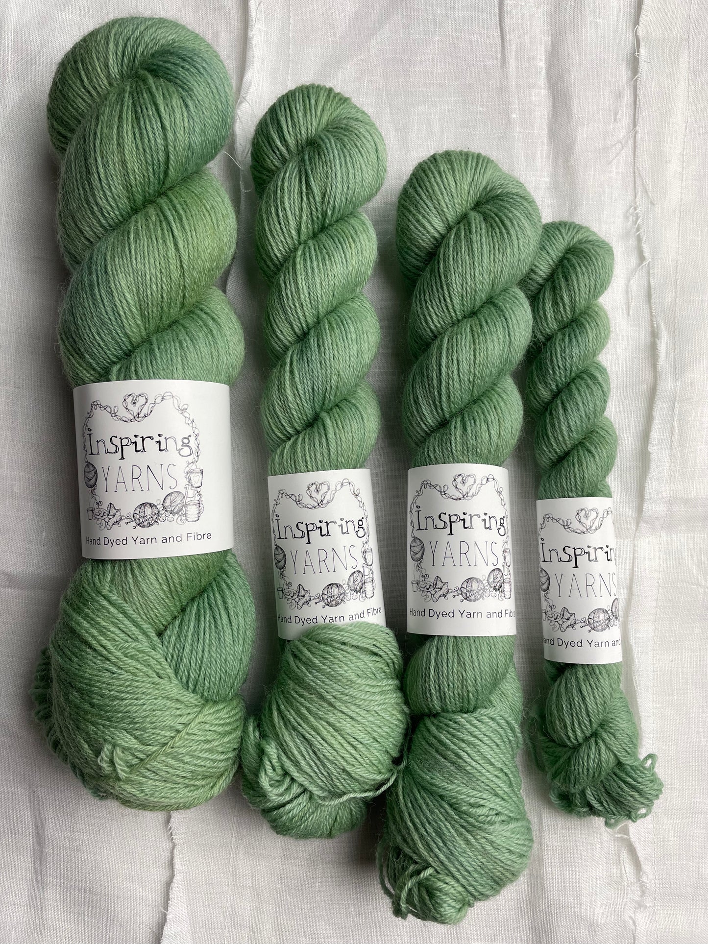 A selection of skeins of soft mint green coloured Highland 4Ply yarn branded Inspiring Yarns on a white linen background.