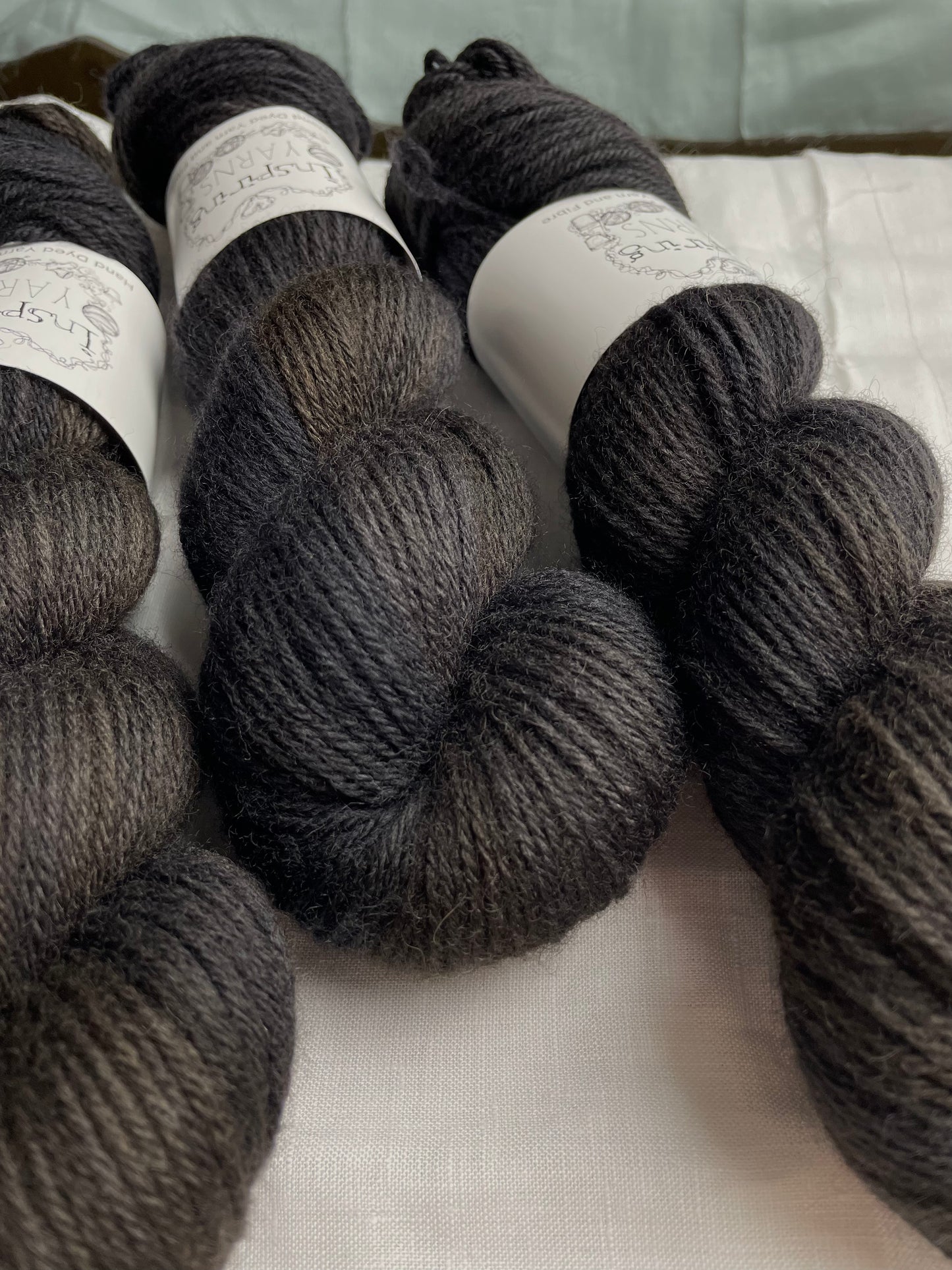 Close up of 3 skeins of tonal black Highland DK yarn on a white linen background.