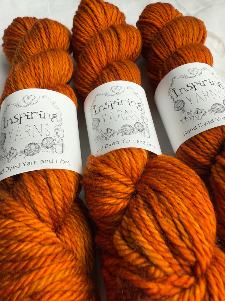 Image shows 3 skeins of merino chunky yarn dyed in a tonal burnt orange colourway.  The yarn has a white band branded Inspiring Yarns.