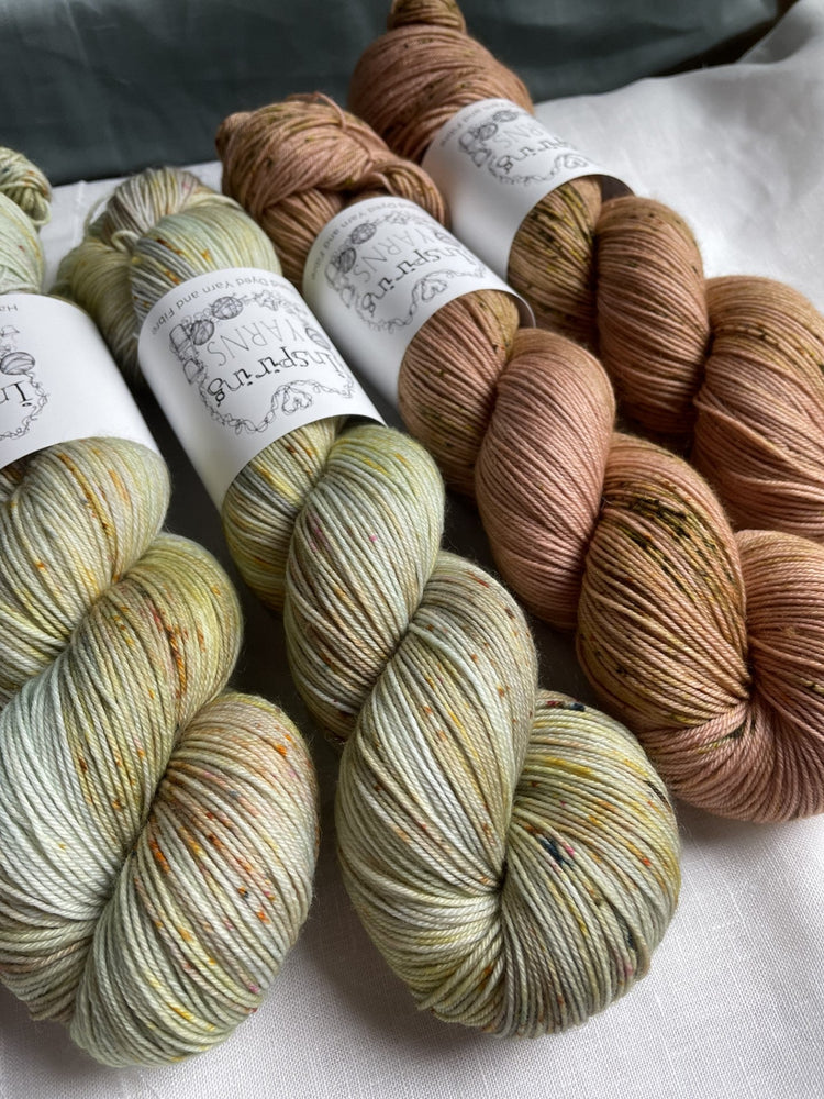 Four skeins of handdyed Merino Smooth Sock in light green and terracotta colours on a white background with Inspiring Yarns branded bands