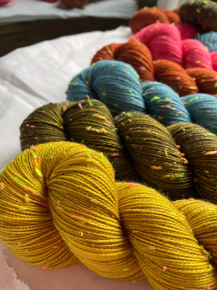 Five skeins of hand dyed yarn in bright colours lie on a white linen cloth.  The yarn has neon coloured neps. 