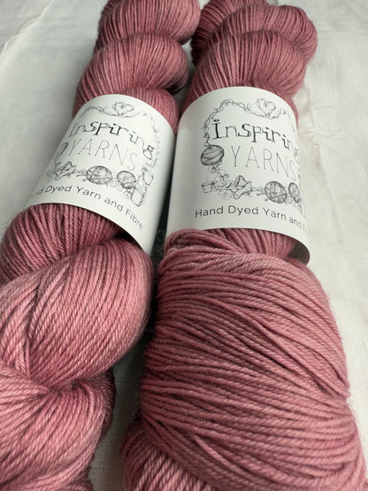 up close of two skeins of light dusty pink yarn with inspiring yarns label on white background.