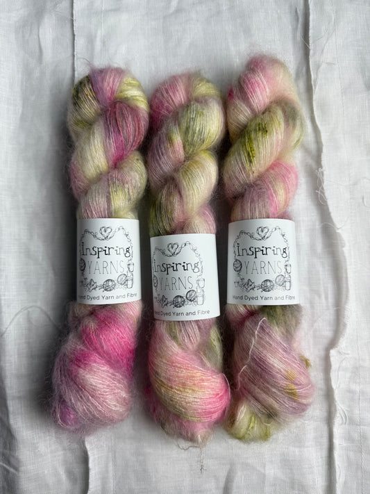 three  skeins of natural base coloured yarn with bright pink and green speckled yarn on a white background with inspiring yarns labels.
