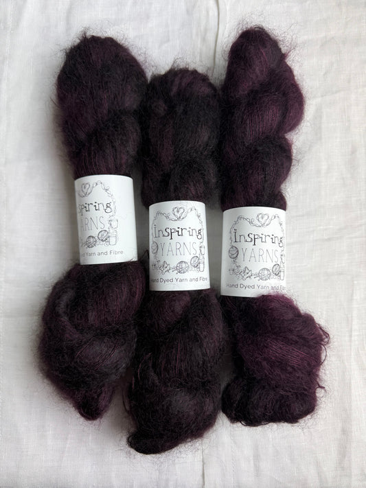Three skeins of dark burgundy mohair yarn labelled Inspiring Yarns on a white linen fabric background