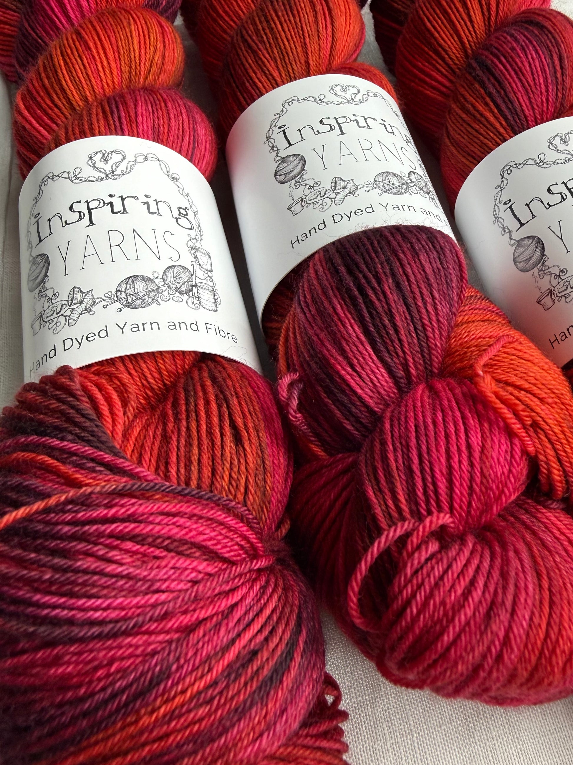 Three skeins of red variegated yarn labelled Inspiring Yarns on a white background