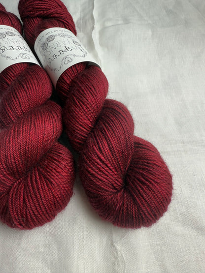 up close two skeins of dark ruby red yarn with inspiring yarns labels around them.