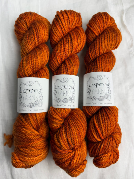 3 skeins of orange yarn with inspiring yarns labels on a white fabric background.