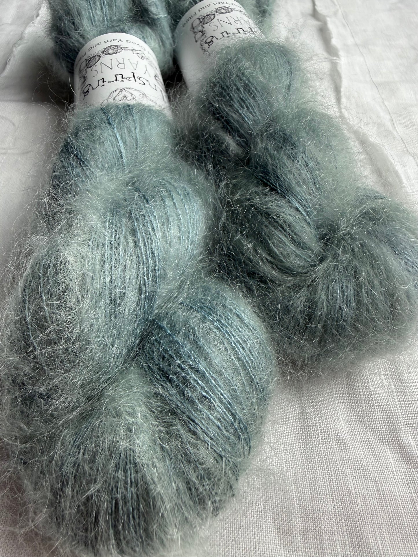 two skeins of mohair silk lace yarn in a pale teal colour and labelled Inspiring Yarns on a white background
