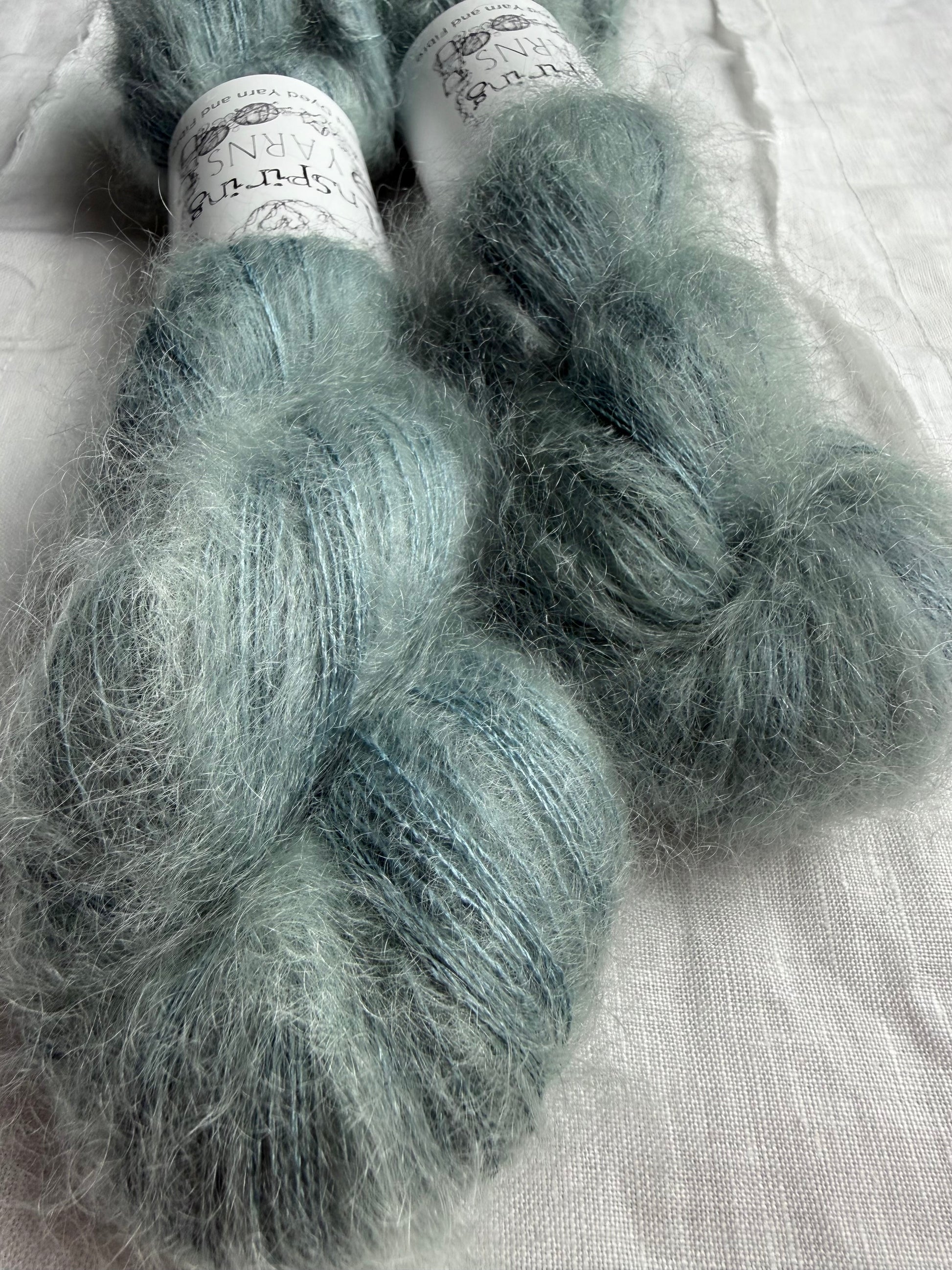 two skeins of mohair silk lace yarn in a pale teal colour and labelled Inspiring Yarns on a white background