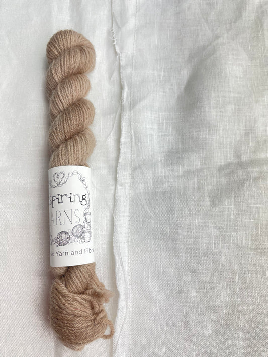 A mini skein of tonal taupe coloured Highland 4Ply yarn branded Inspiring Yarns on a white linen background.