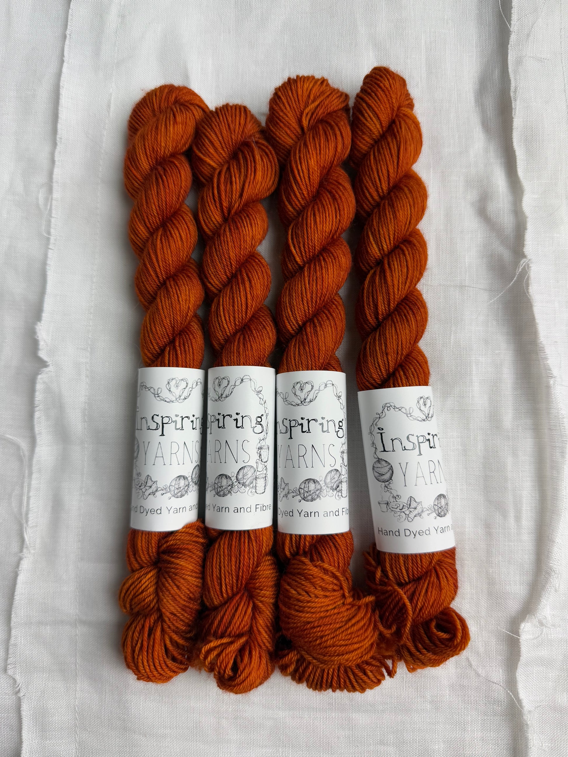 four skeins of tonal burnt orange yarn with inspiring yarns labels on white background. 