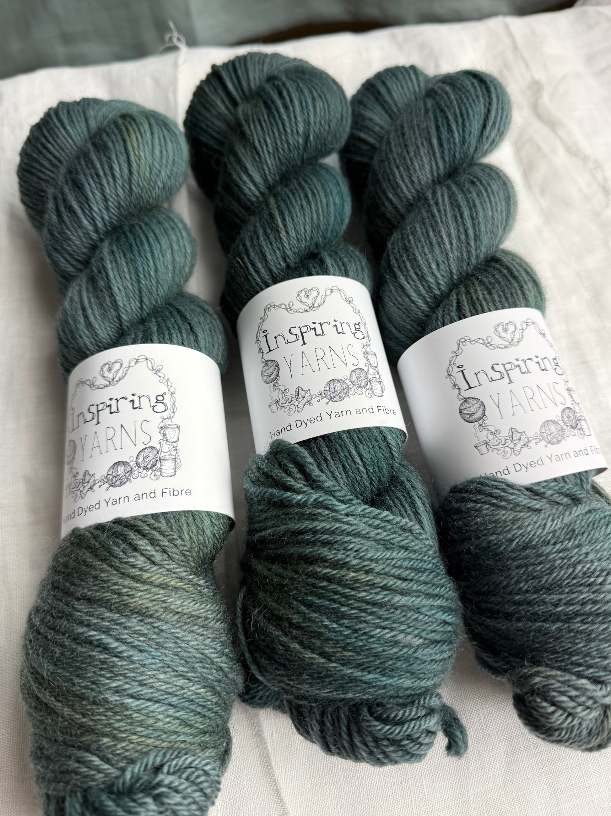 Three skeins of dark green tonal yarn labelled Inspiring Yarns on a white background