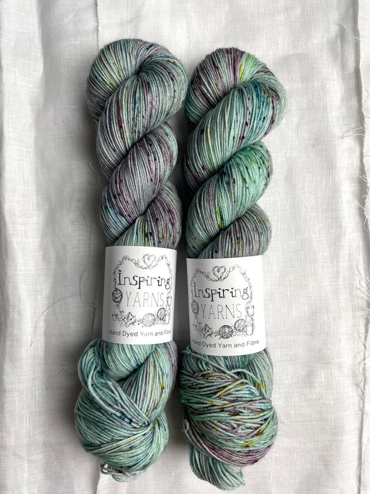 Two skeins of merino smooth sock yarn in a light teal colour with coloured speckles labelled Inspiring Yarns on a white linen background. 