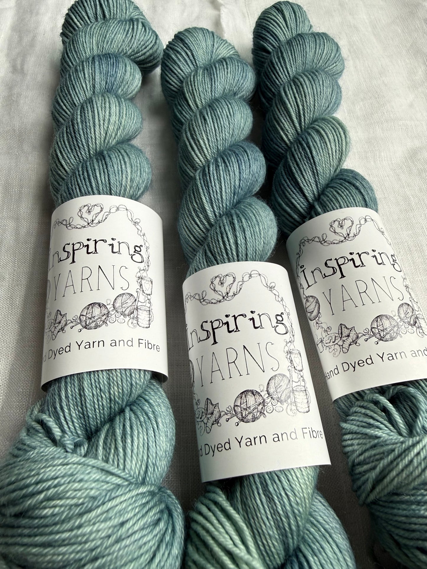 Three skeins of teal yarn with 'Inspiring Yarns' labels on a white background
