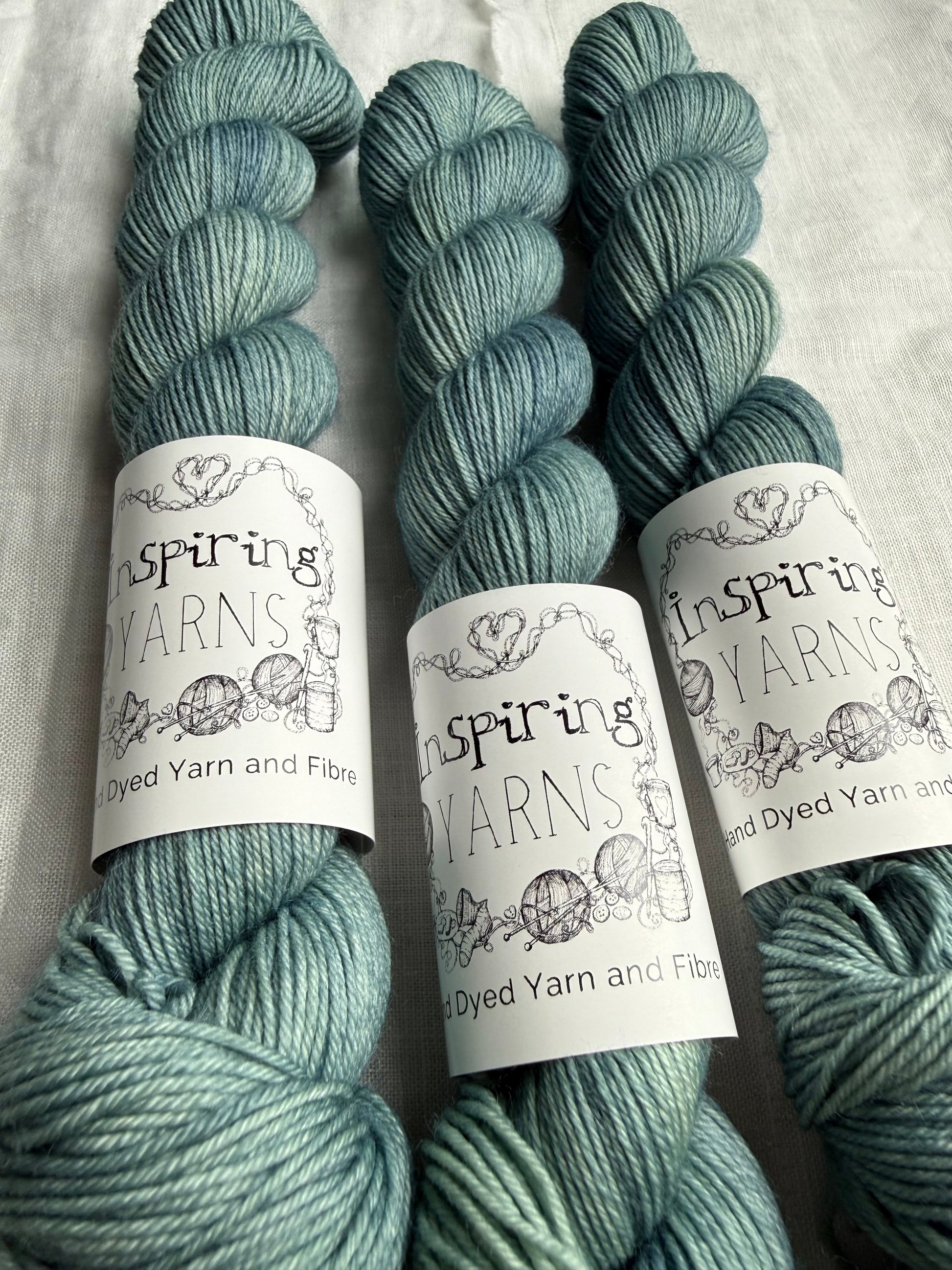 Three skeins of teal yarn with 'Inspiring Yarns' labels on a white background