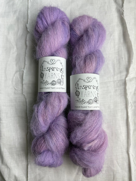two skeins of light pink and lilac yarn with inspiring yarns labels and white background 