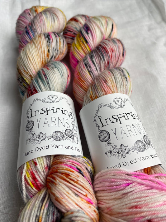 Two skeins of multi coloured speckled Merino Smooth Sock labelled InspiringYarns lies on a white linen background.