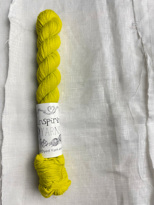 A bright acid yellow coloured mini skein of Merino Smooth Sock yarn branded  Inspiring Yarns on a white linen fabric background. 