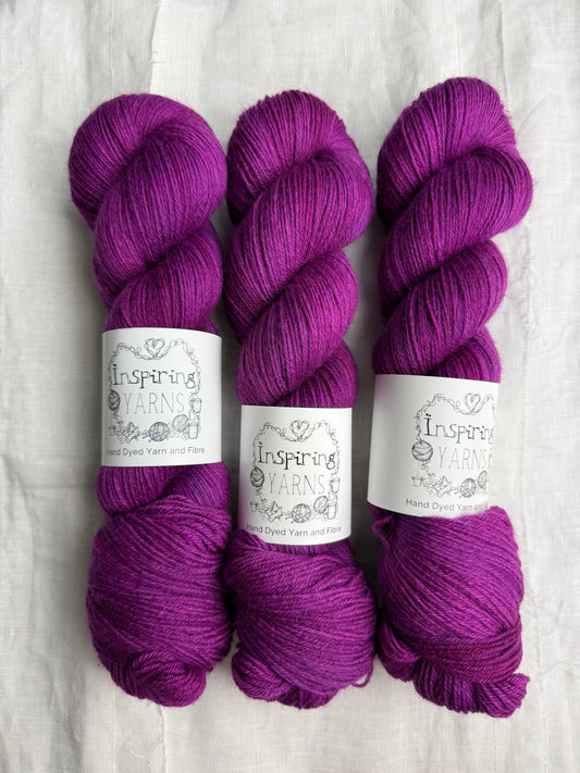 Three skeins of fuchsia tonal yarn labelled Inspiring Yarns on a white background