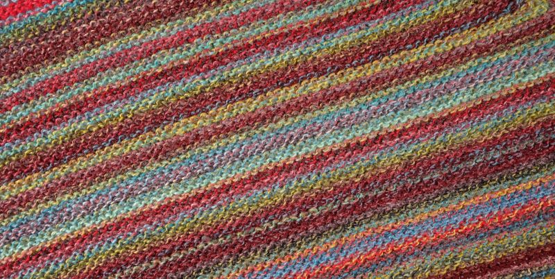 Image shows knitted swatch for Schoppel Zauberball Crazy 4ply/sock.  The colour is 2429 Chaange of Scenery/Tapetenweschsel, with shades of coral, yellow, blue/grey.