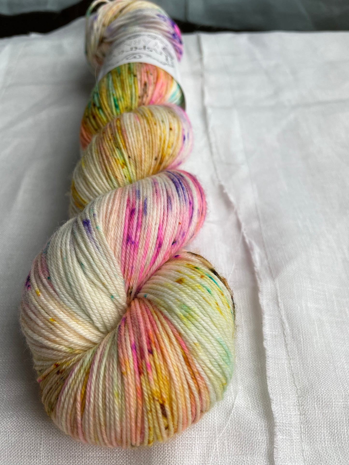 up close of a skein of natural coloured yarn and multicoloured speckles with inspiring yarns label on a  white background.