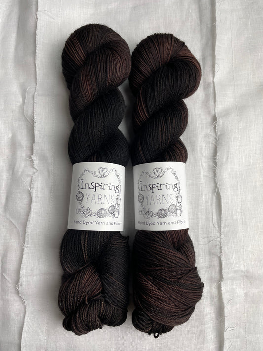 Two skeins of variegated dark brown black Merino Smooth Sock yarn labelled Inspiring Yarns on a white linen background