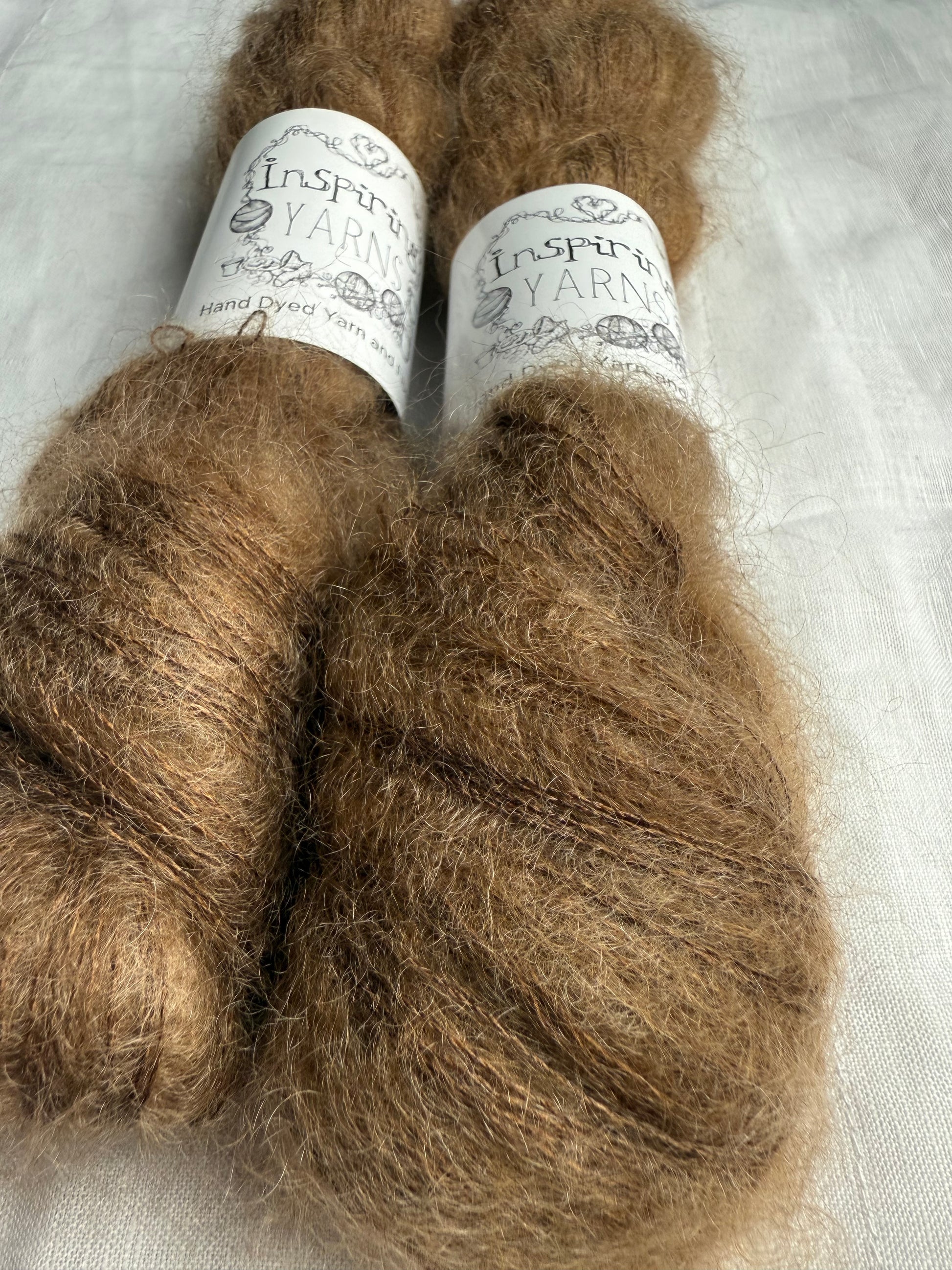 two skeins of a tonal light brown mohair with inspiring yarns label up close on white background.