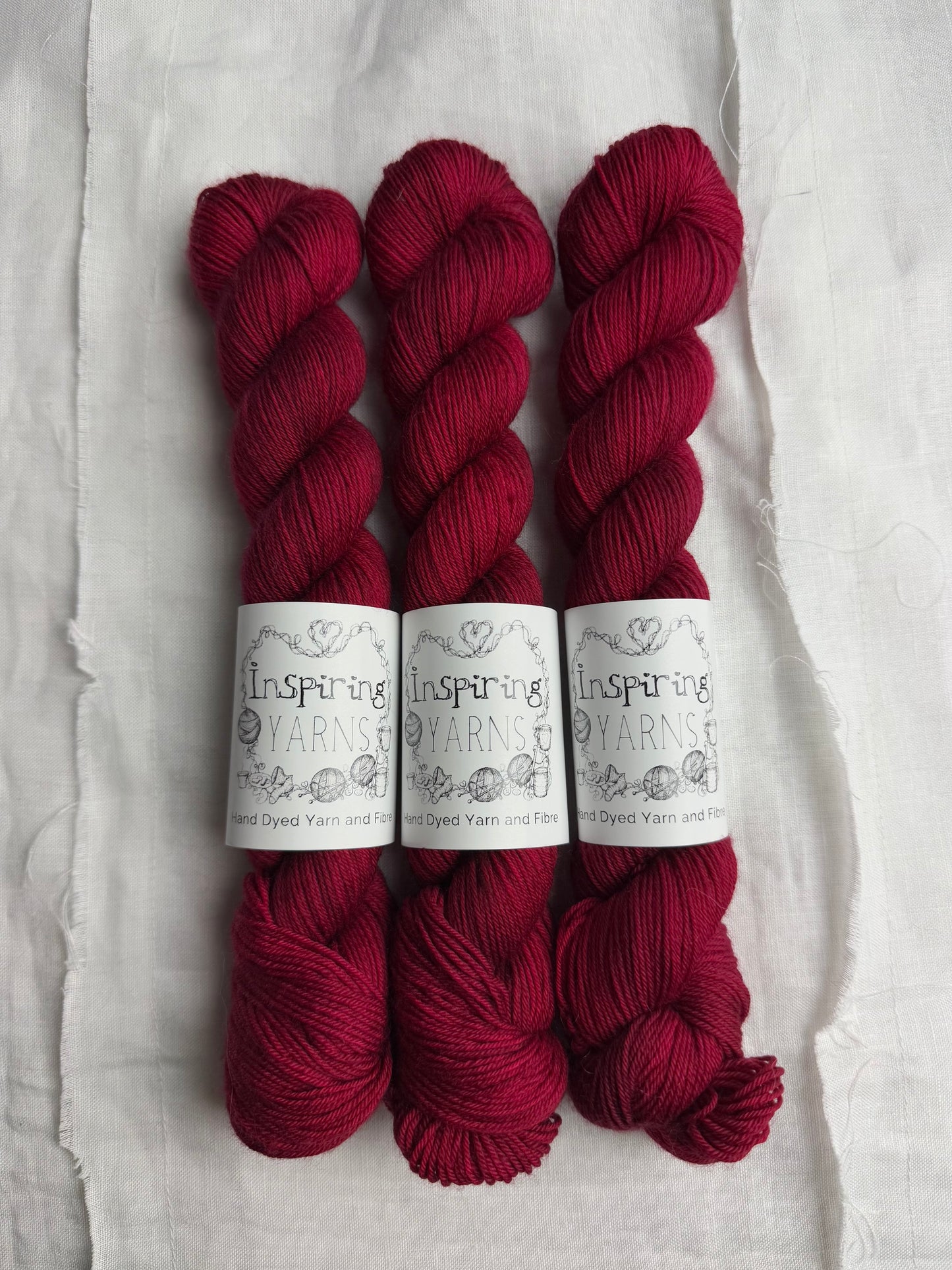 three skeins of dark ruby red yarn on a white background and inspiring yarns label around them.