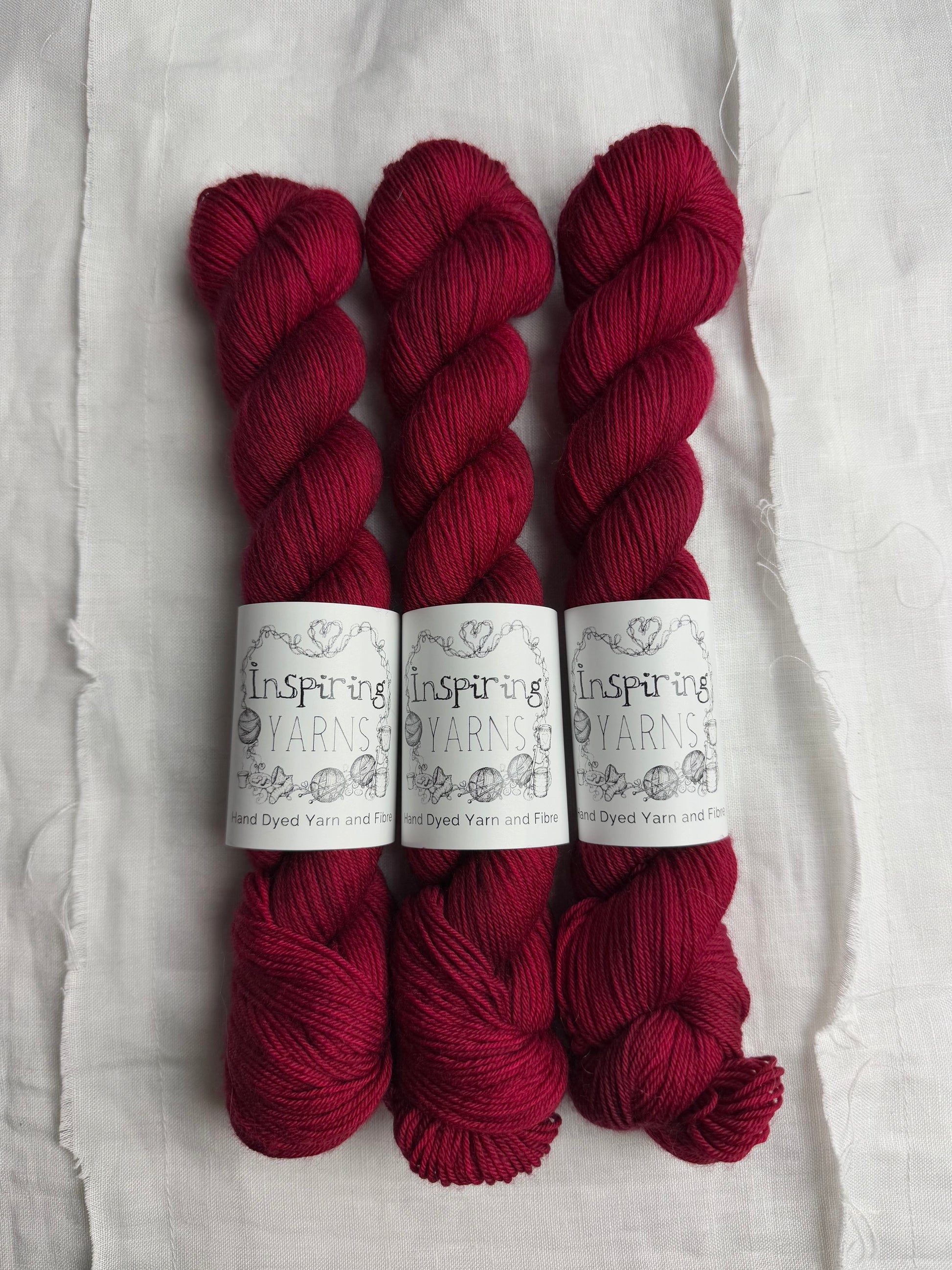 three skeins of dark ruby red yarn on a white background and inspiring yarns label around them.