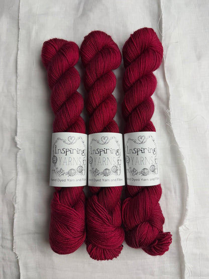 three skeins of dark ruby red yarn on a white background and inspiring yarns label around them.