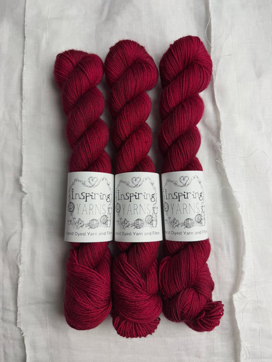 three skeins of dark ruby red yarn on a white background and inspiring yarns label around them.