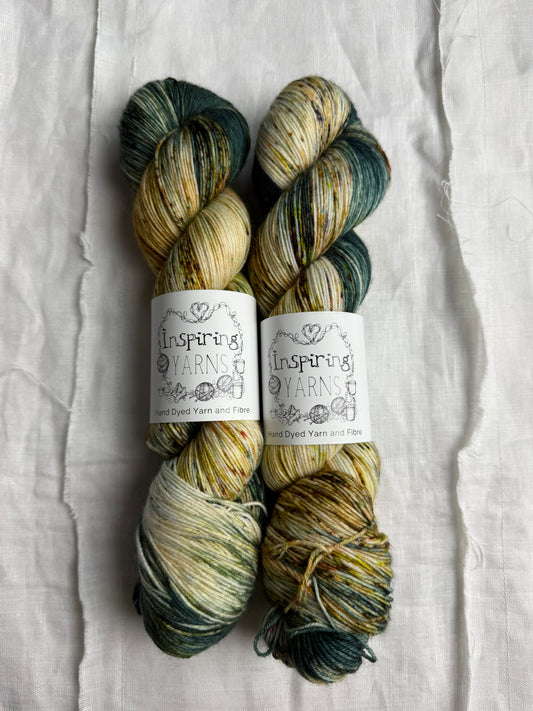 two skeins of yarn with neatrals and teals with coloured speckles on a white background and inspiring yarns label.