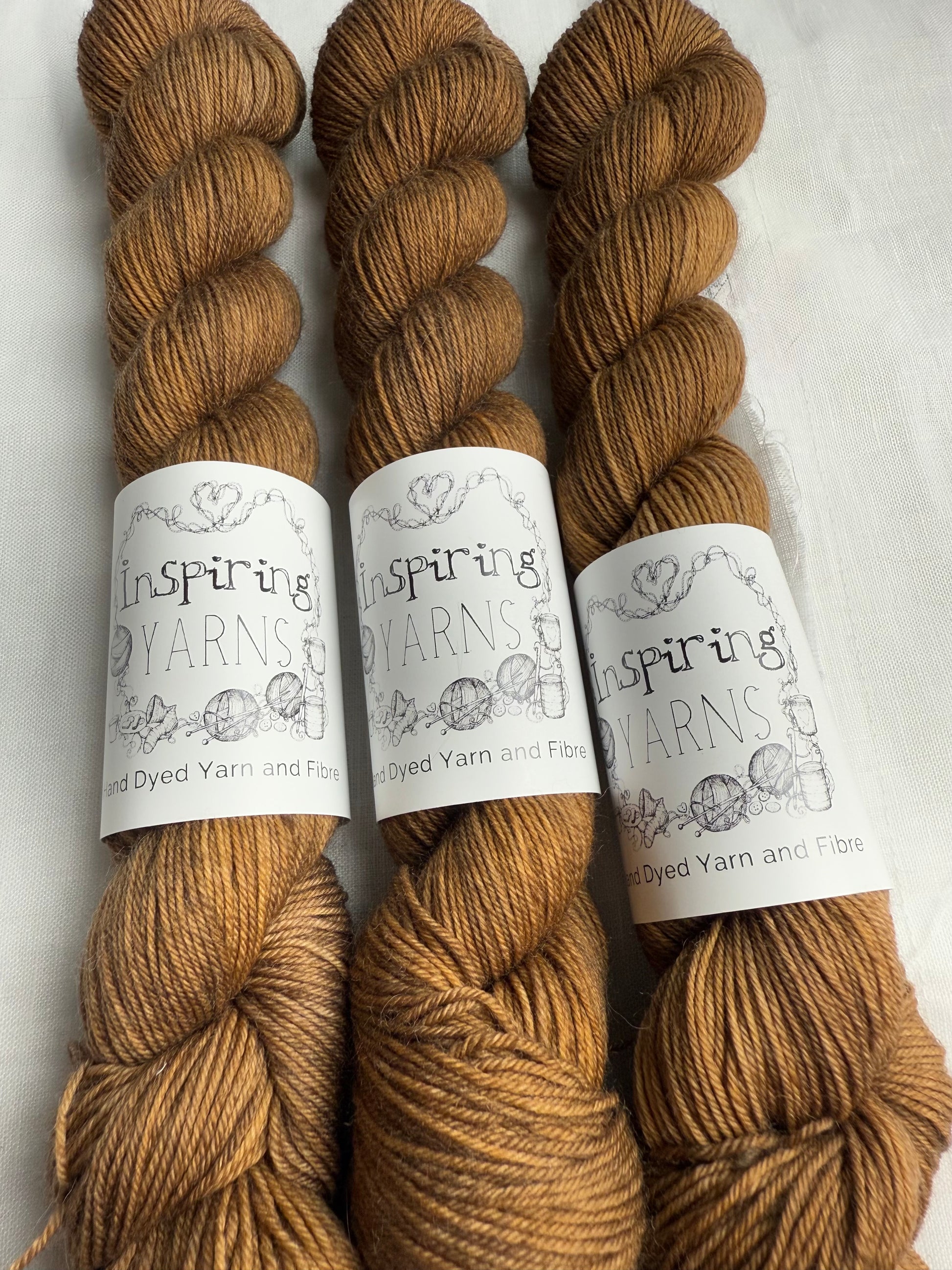 Three skeins of light tonal  brown yarn with 'Inspiring Yarns' labels on a white background.