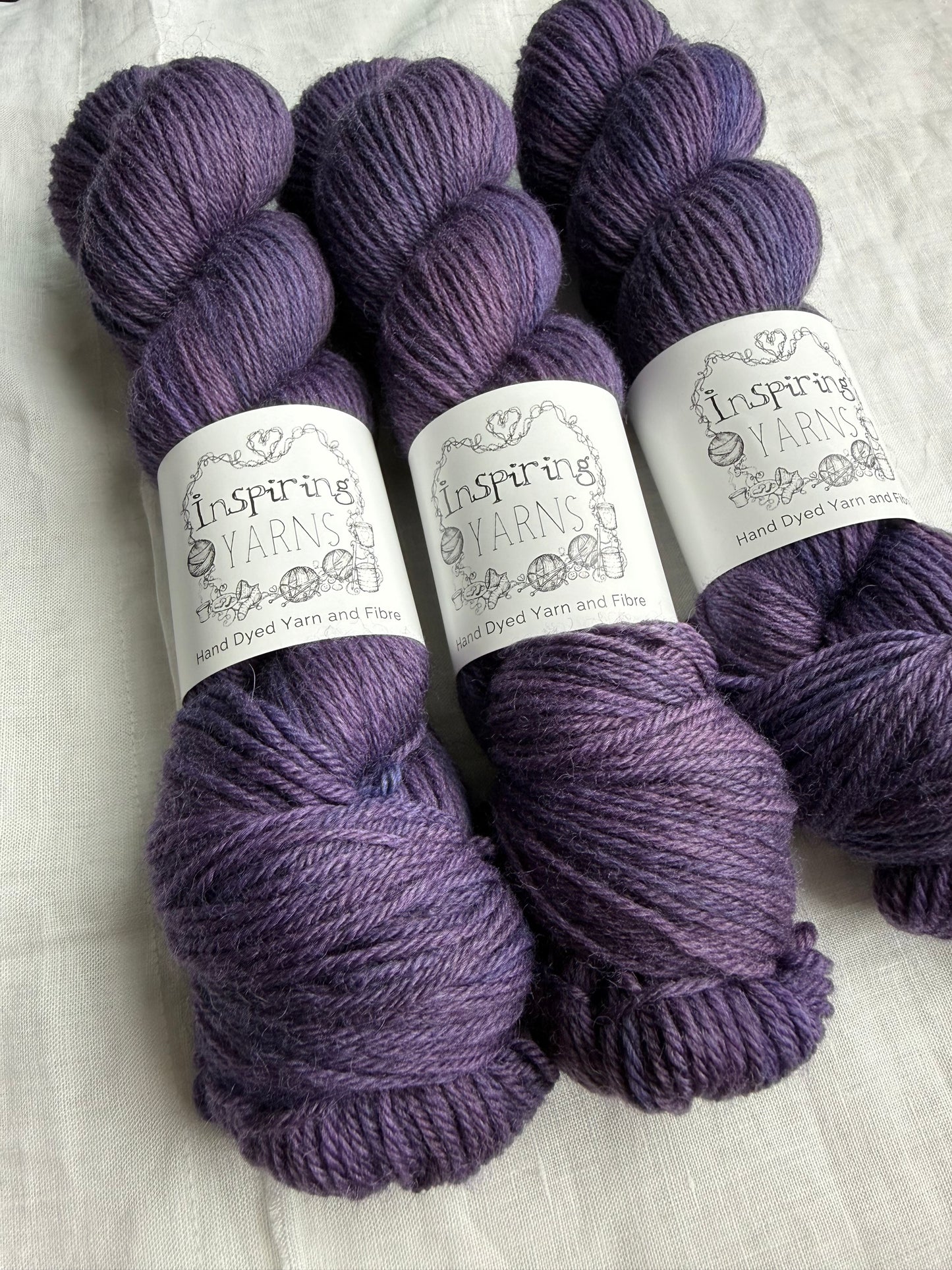 Three skeins of purple tonal yarn labelled Inspiring Yarns on a white background