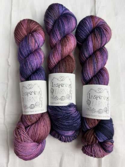 three skeins of violet, purple and brown variegated yarn with white background and inspiring yarns label.
