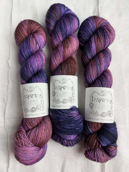 three skeins of violet, purple and brown variegated yarn with white background and inspiring yarns label.