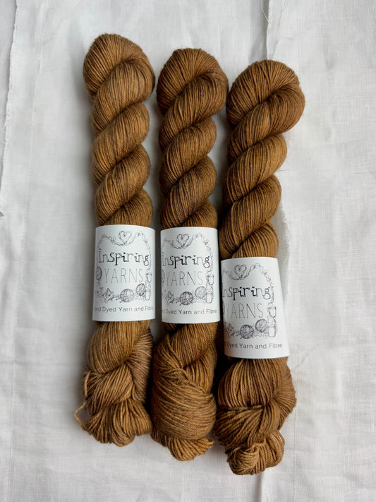 Three skeins of light  brown tonal  yarn with inspiring yans labels on  a white background.