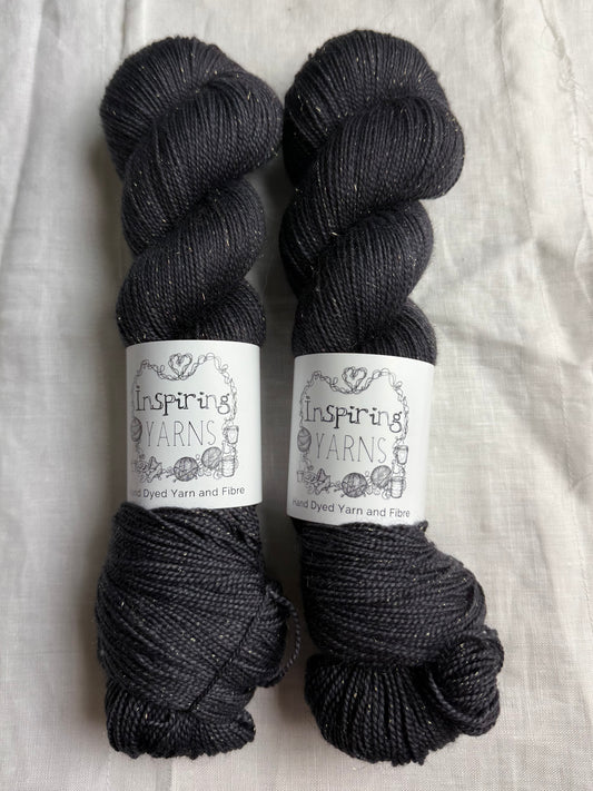 Two skeins of tonal charcoal black yarn with Inspiring Yarns labels on a light fabric background.