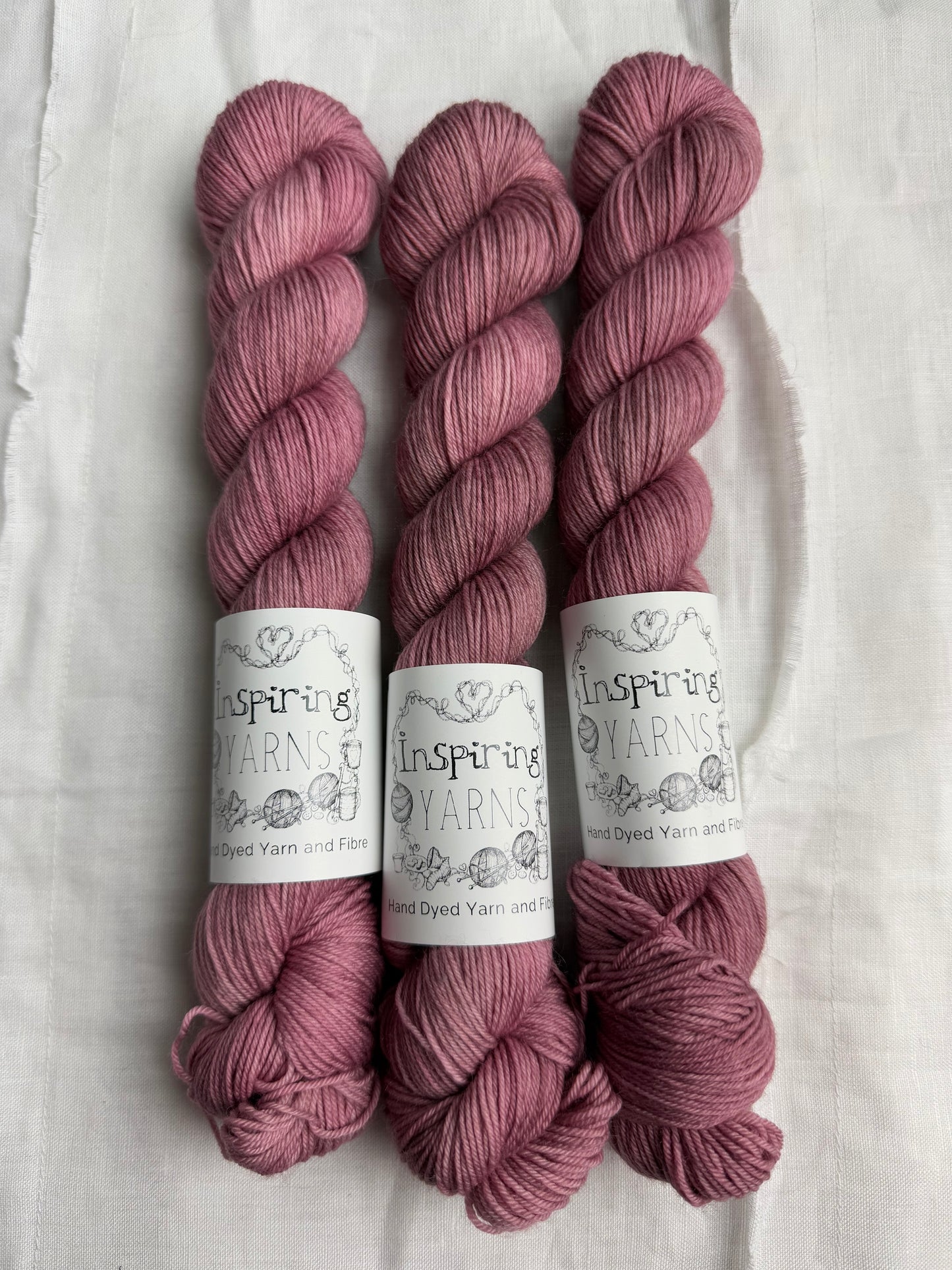 Three skeins of dusty  pink yarn with inspiring yarns  labels on a white background.