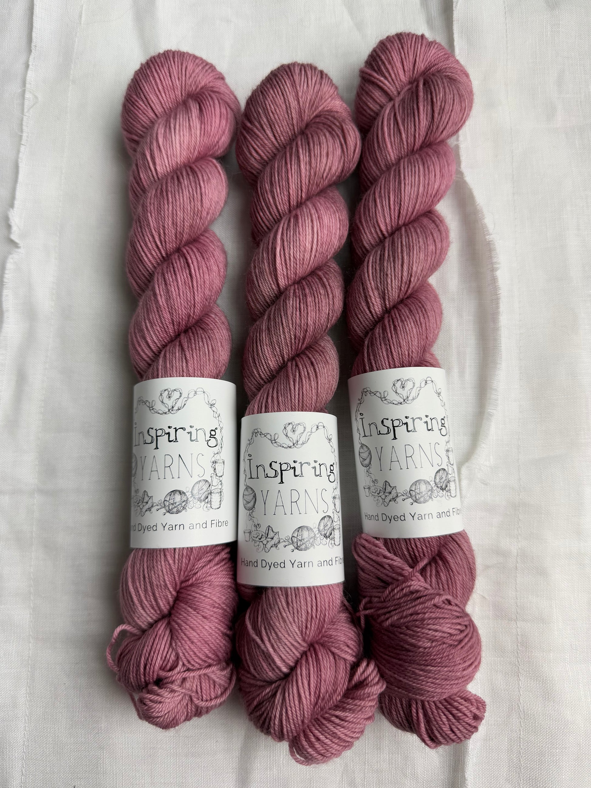 Three skeins of dusty  pink yarn with inspiring yarns  labels on a white background.