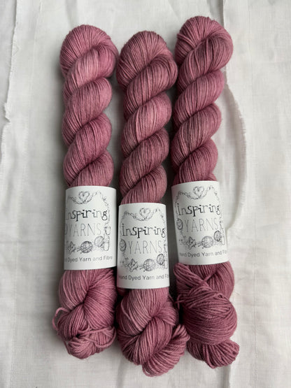 Three skeins of dusty  pink yarn with inspiring yarns  labels on a white background.