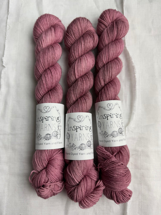 Three skeins of dusty  pink yarn with inspiring yarns  labels on a white background.