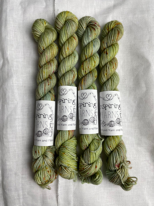Four mini skeins of Faded Glory, a pale green with speckles coloured Merino Smooth Sock, labelled Inspiring Yarns on a white linen background. 