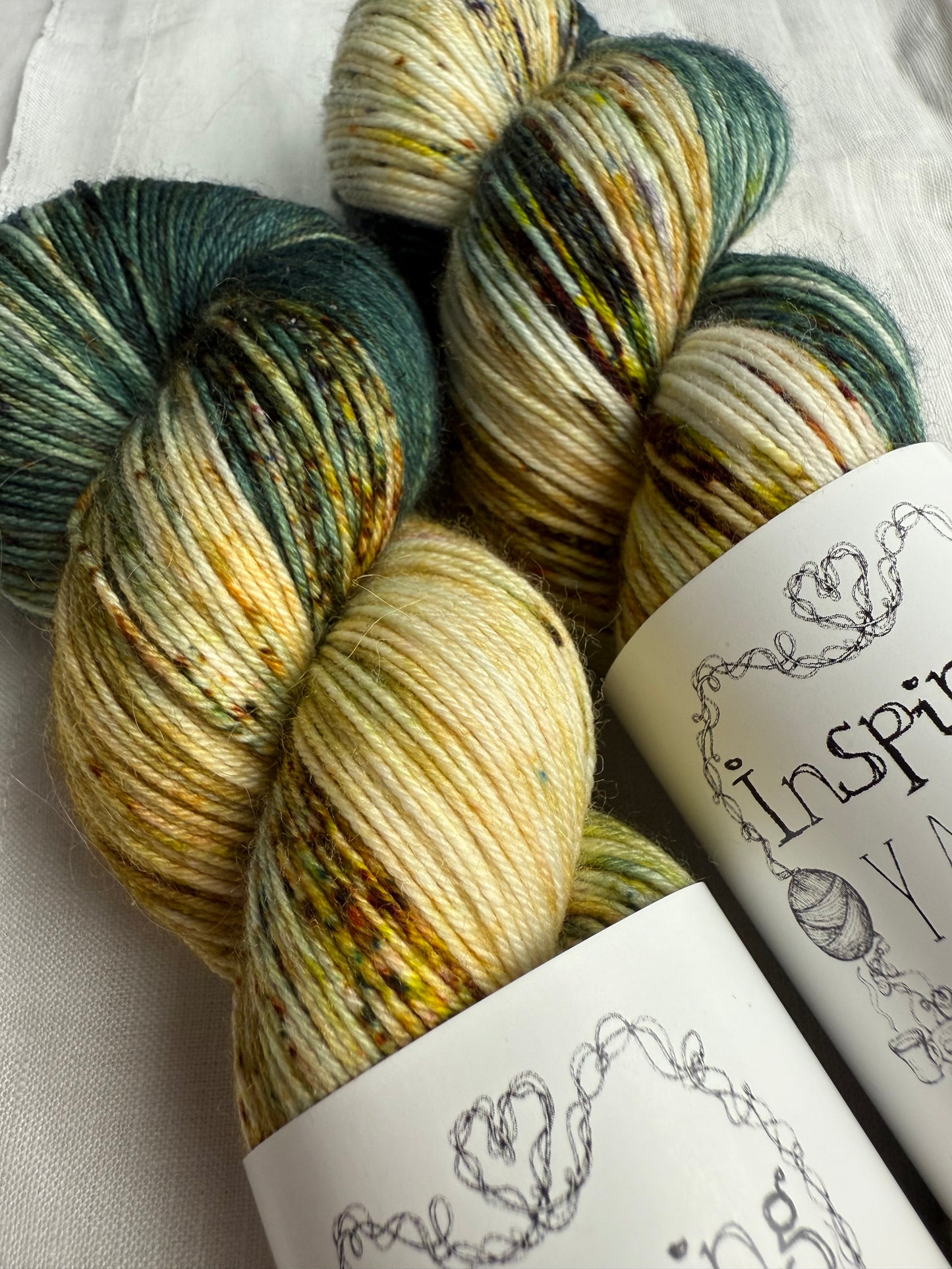 up close of two skeins of yarn with natural and teal base with multicoloured speckles on a white background.