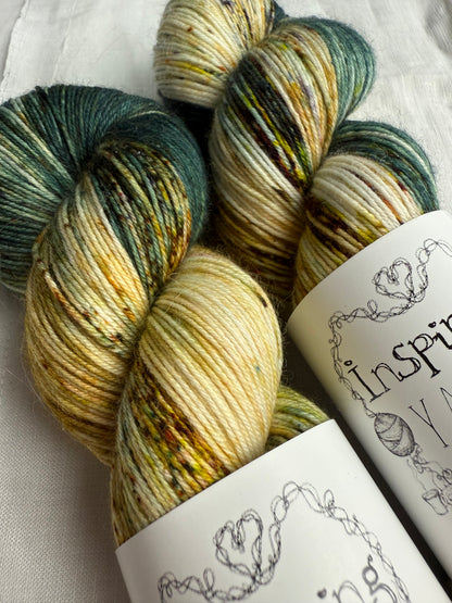 up close of two skeins of yarn with natural and teal base with multicoloured speckles on a white background.