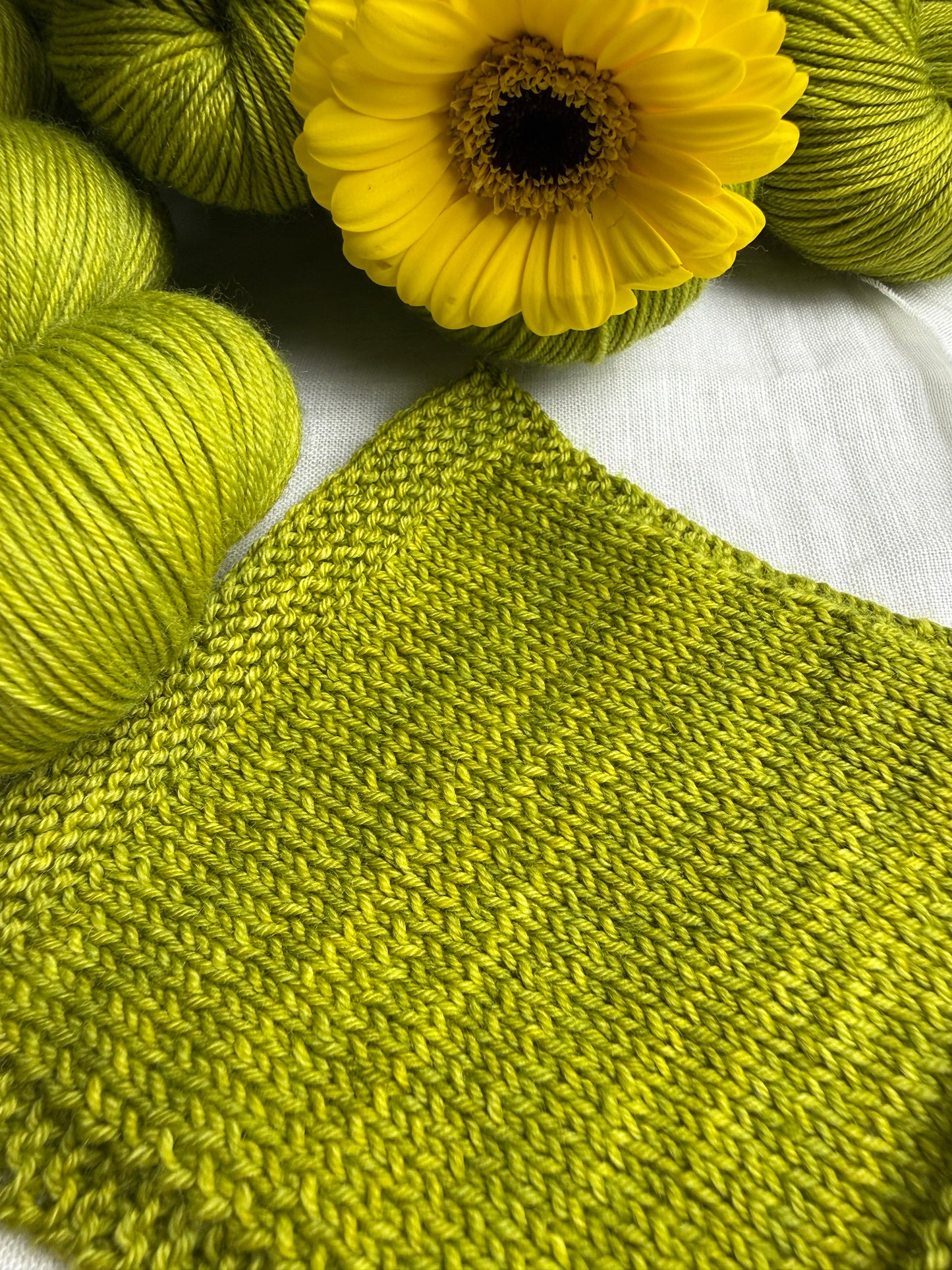 Green knitted fabric and yarn with a yellow flower on a white background