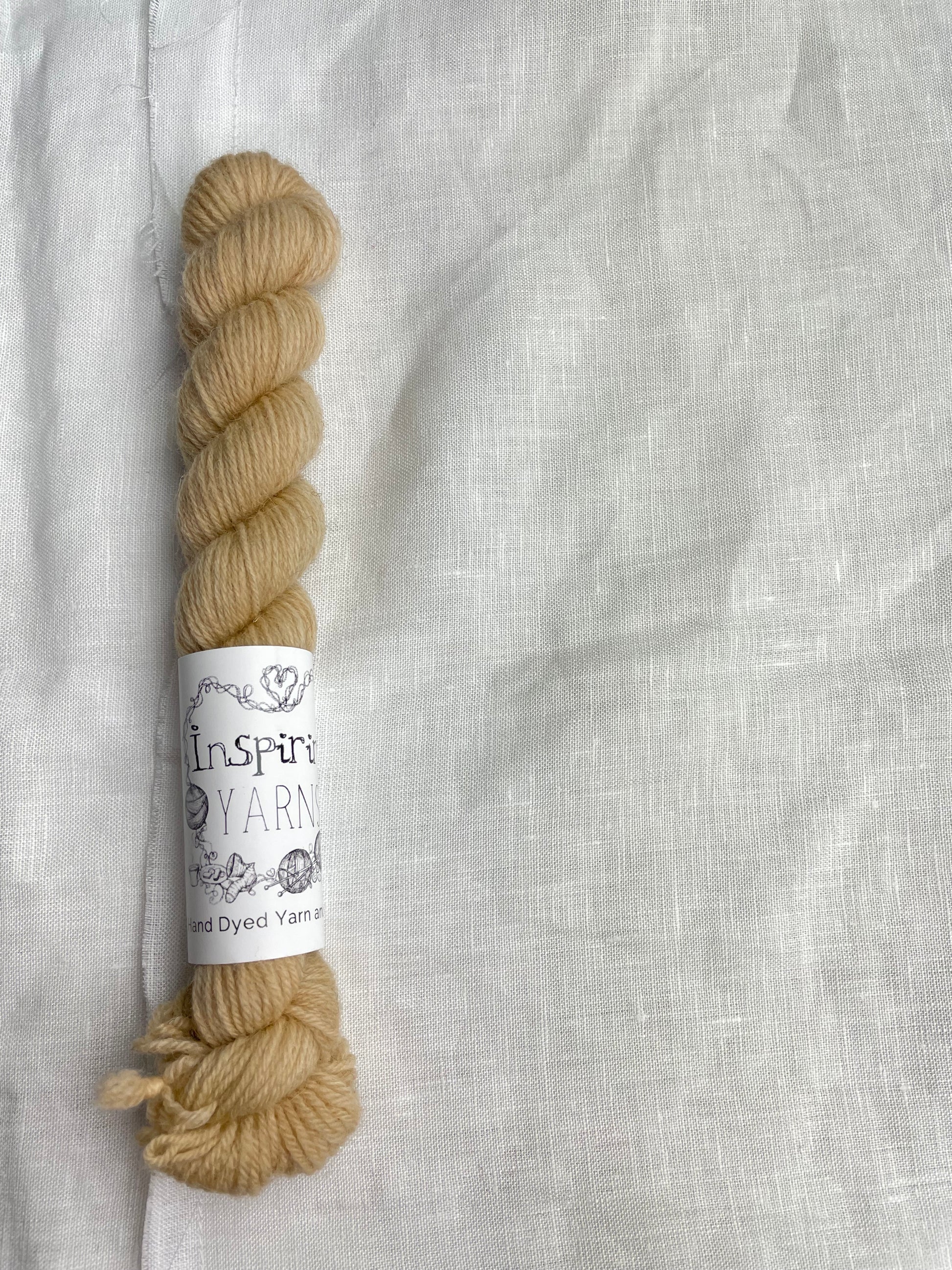 A mini skein of tonal golden caramel coloured Highland 4Ply yarn branded Inspiring Yarns on a white linen background.